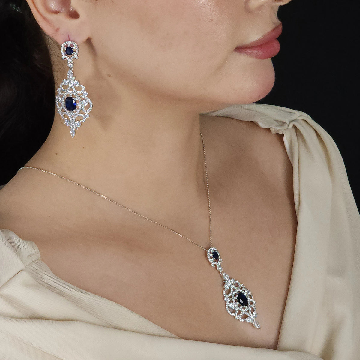 طقم مرصع بأحجار الزركون الشفافة، مع أحجار أزرق ملكية ذات اللون الكحلي العميق Jewelry set adorned with clear zircon stones and deep navy-blue royal blue stones.